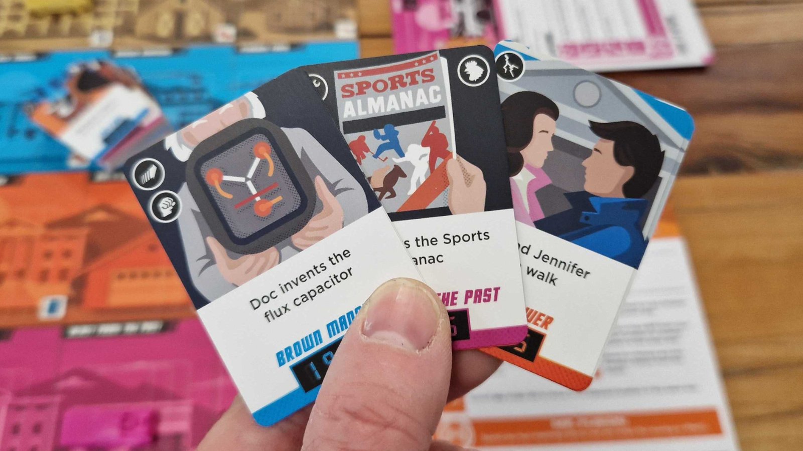 A hand holds up cards in front of the Back to the Future: Dice Through Time board