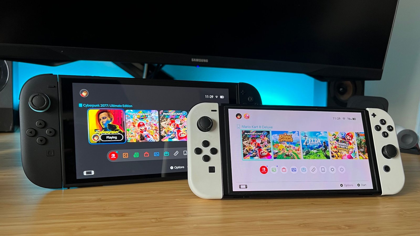 Nintendo Switch 2 and Nintendo Switch OLED on a wooden desk with blue backlighting