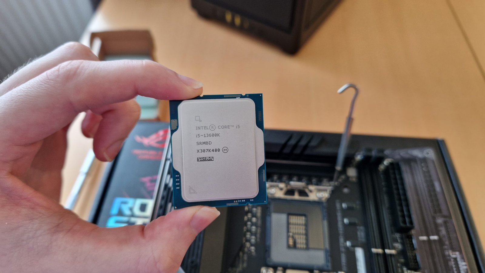 Intel Core i5-13600K review image of the processor being held face up to the camera above a motherboard