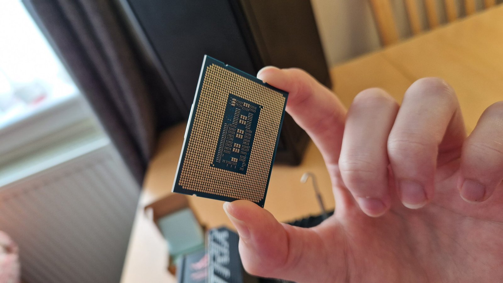 Intel Core i5-13600K review image of the CPU's backside being held above a motherboard by the reviewer