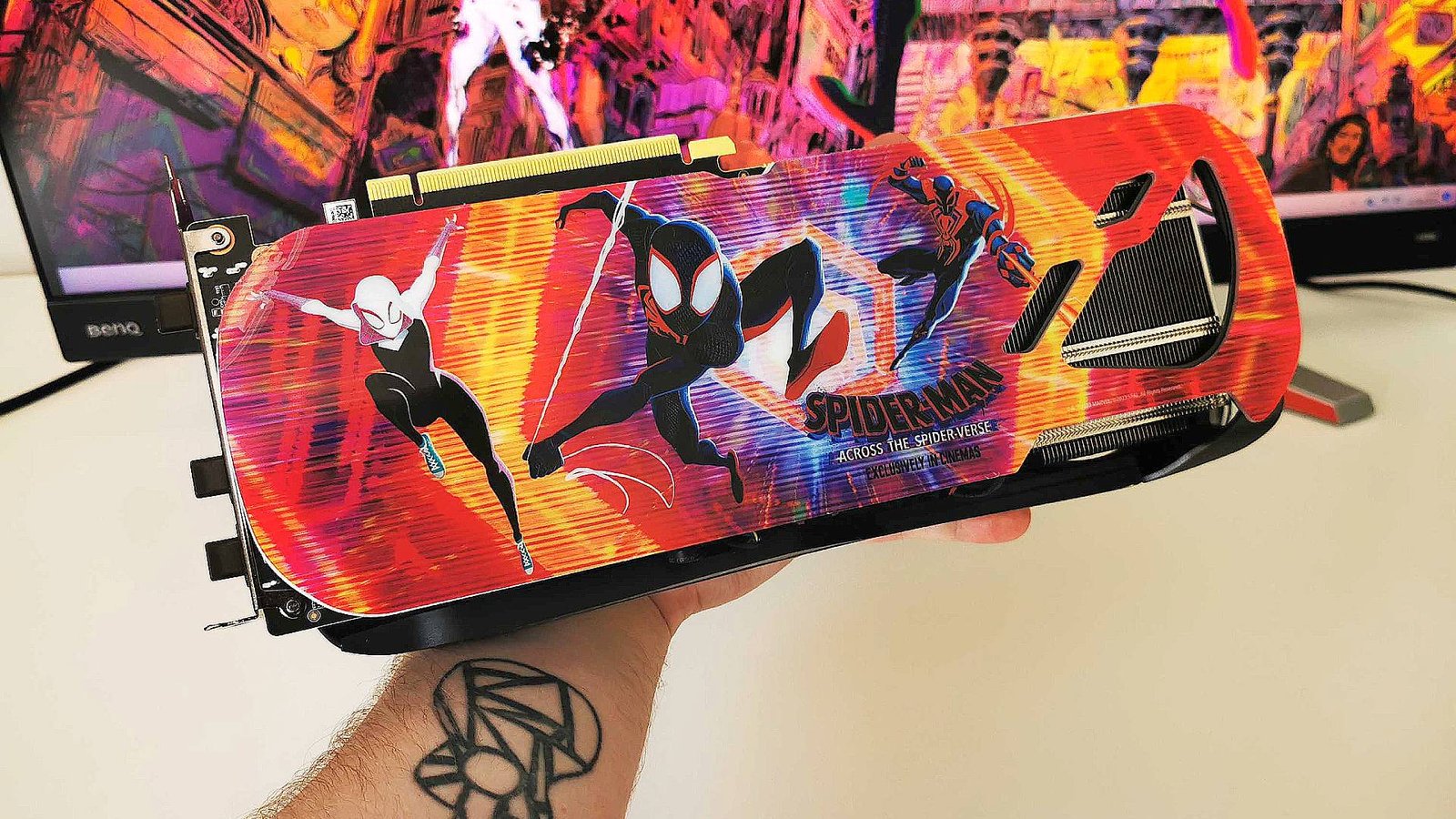 Hand holding Zotac RTX 4070 Ti Across the Spider-Verse themed graphics card next to white desk