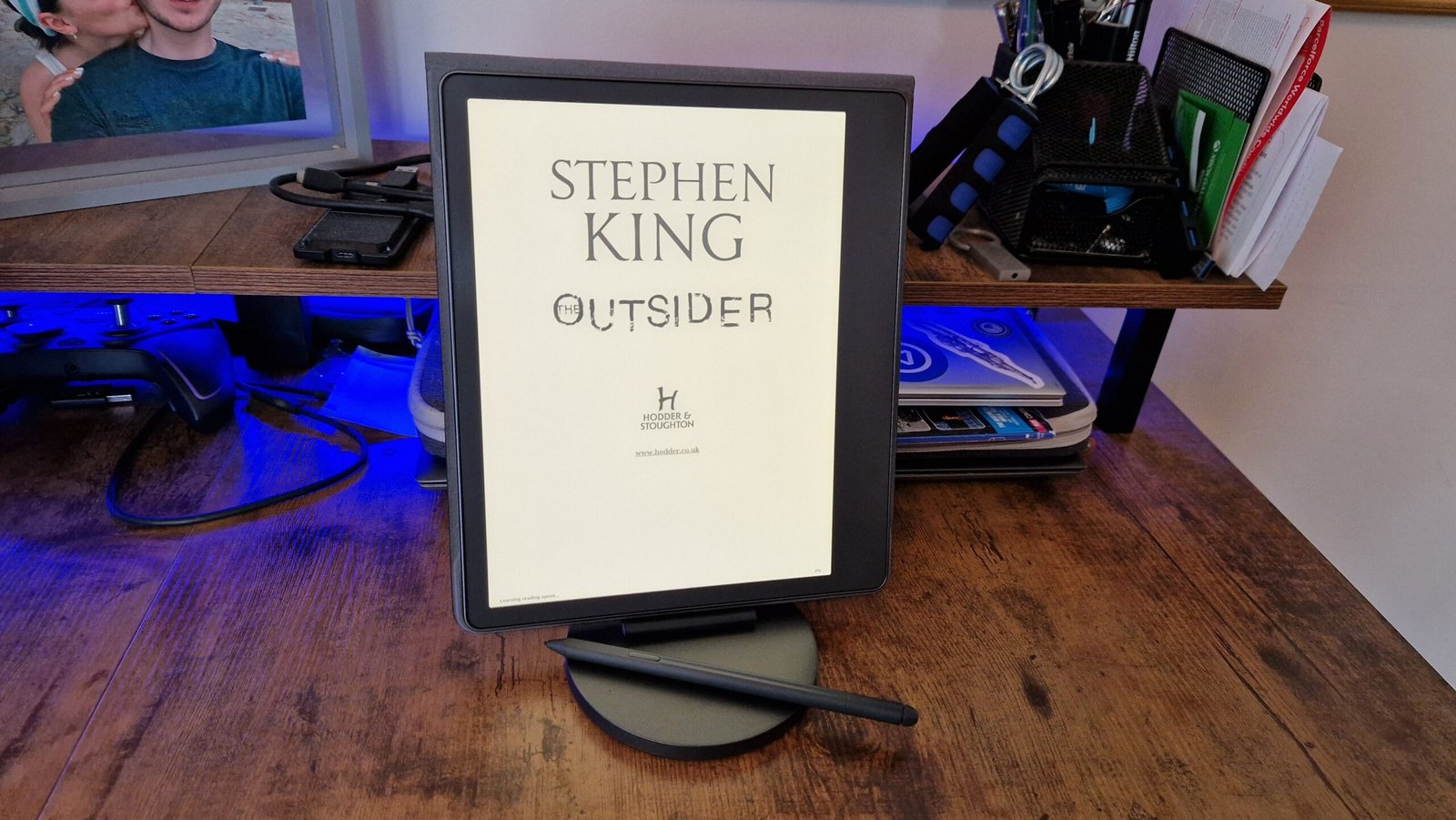 A Kindle Scribe propped up on a desk in front of blue lighting
