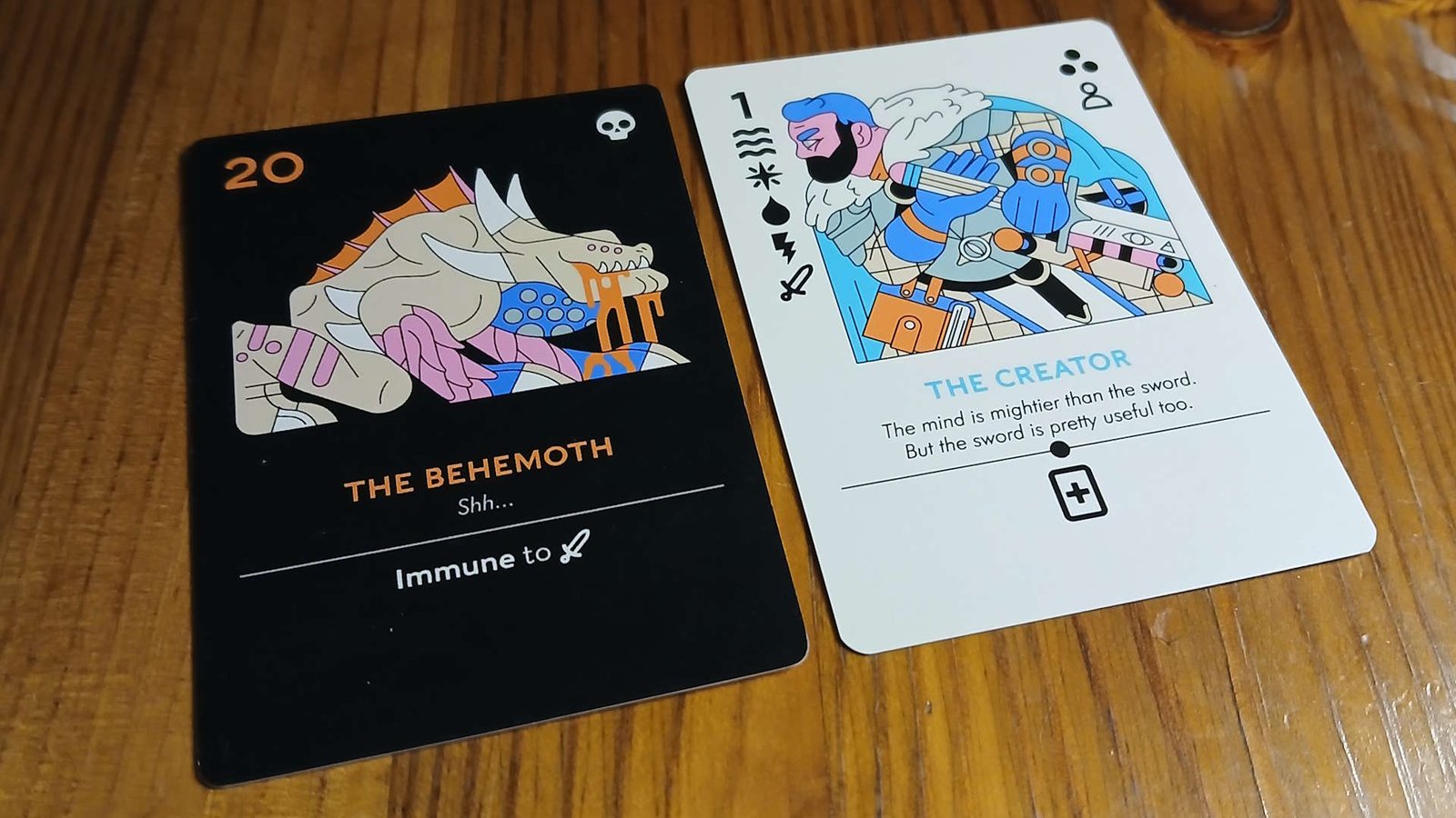 A card showing 'The Behemoth' faces a 'The Creator' card on a wooden table