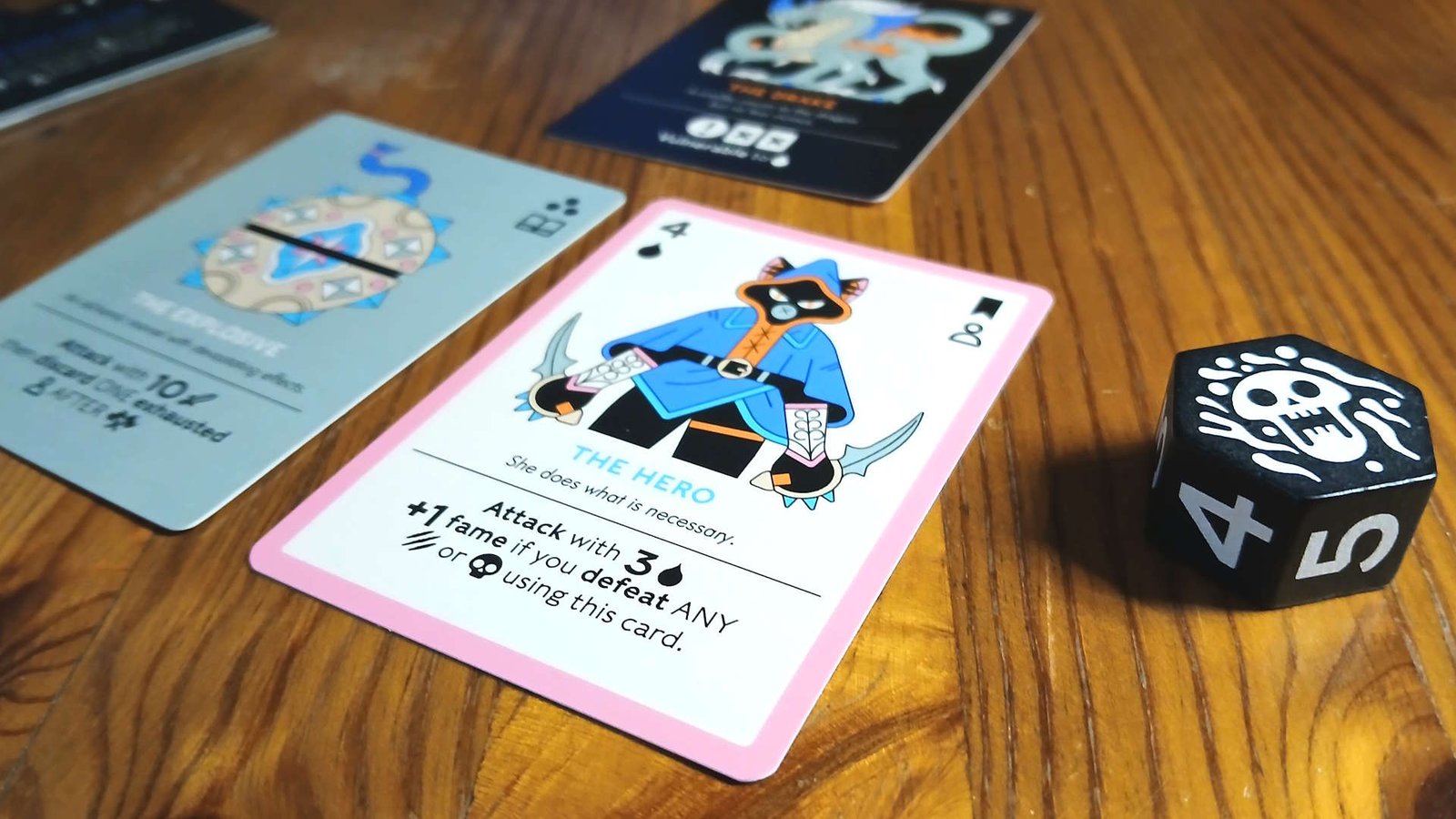 Three cards and a skull token with numbers on the side, sitting on a wooden table