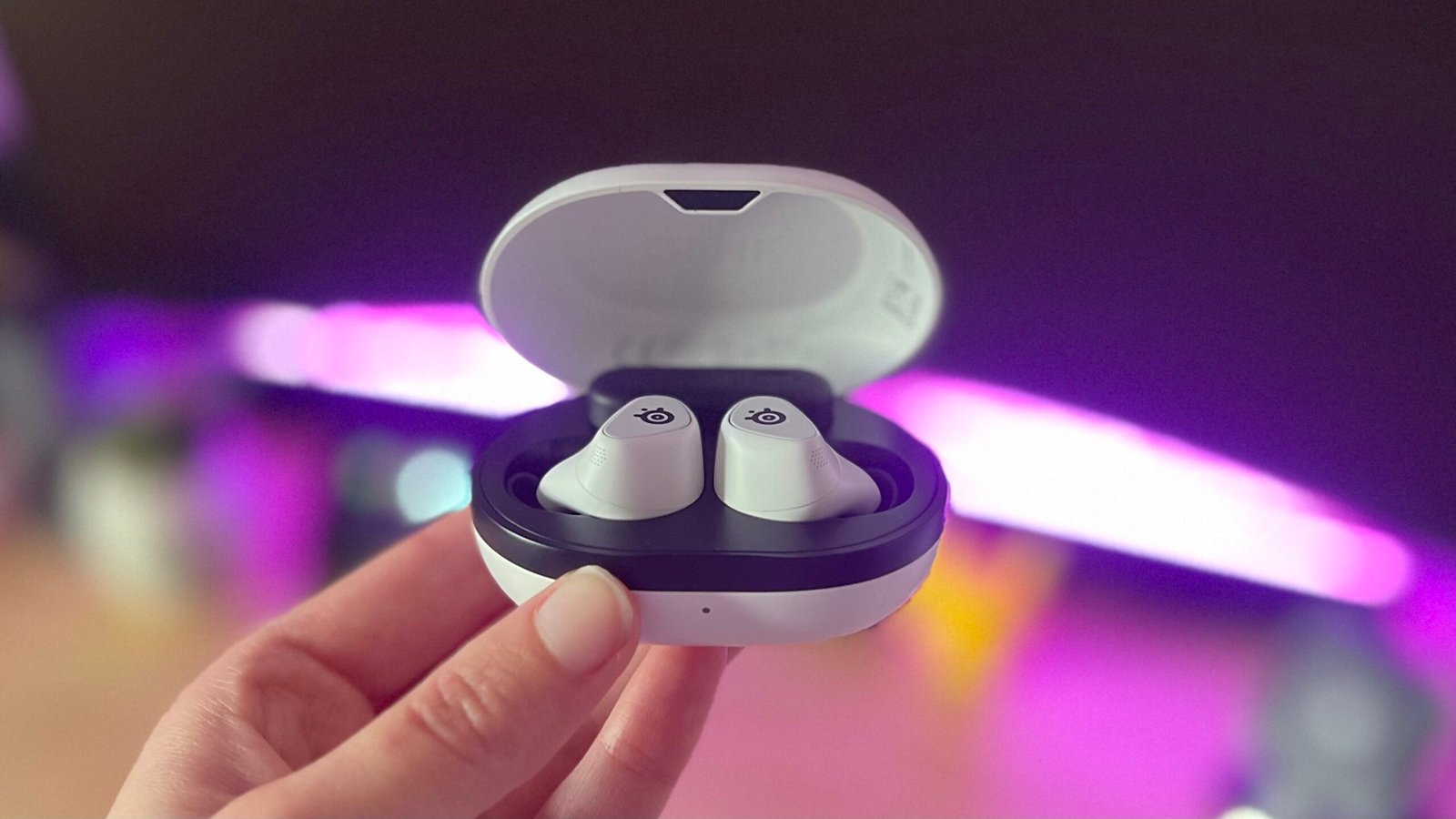 Reviewer's hand holding SteelSeries Arctis Game Buds in charging case