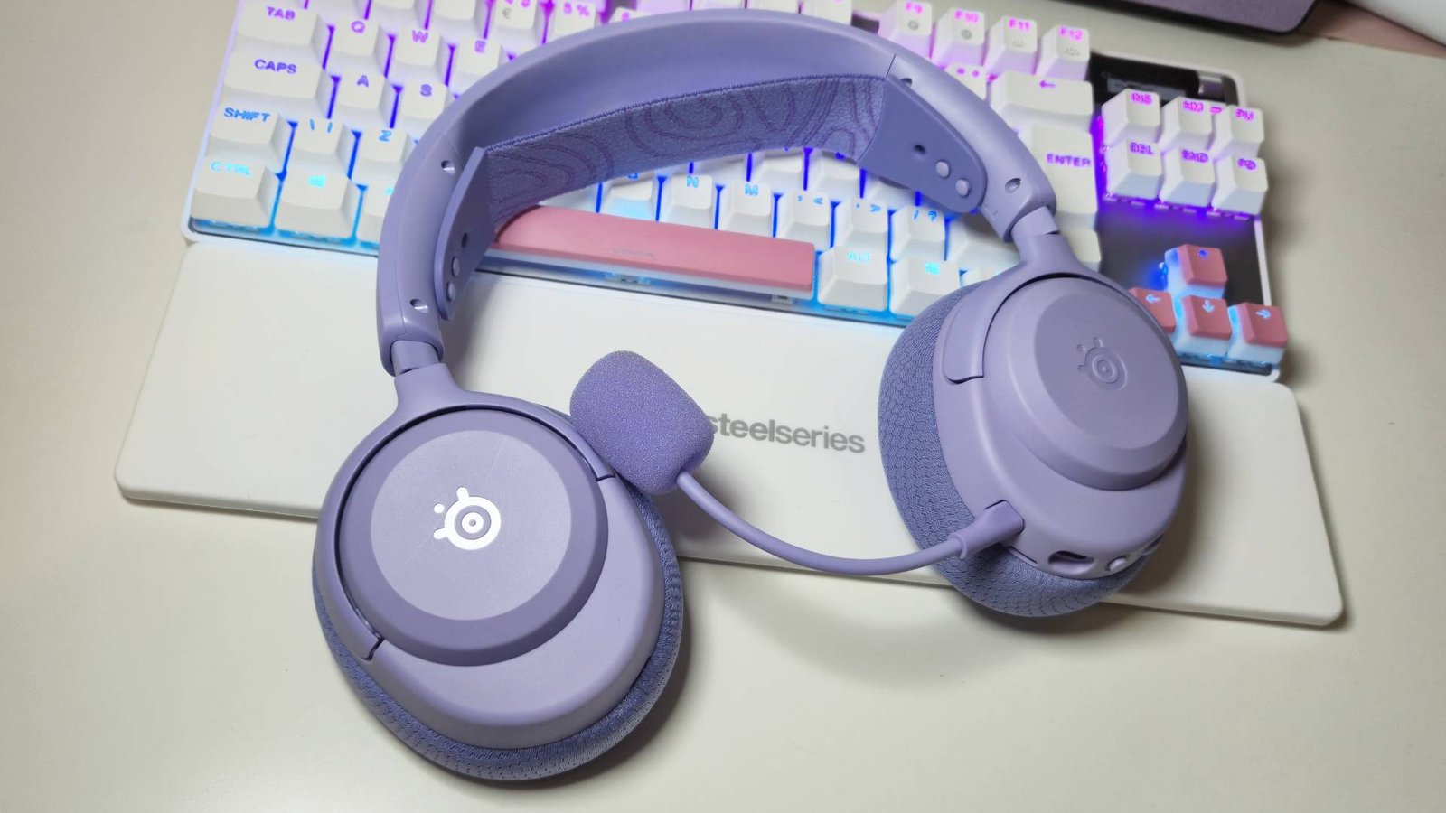 Photos of the SteelSeries Arctis Nova 3 Wireless gaming headset in Lavender on a white desk.