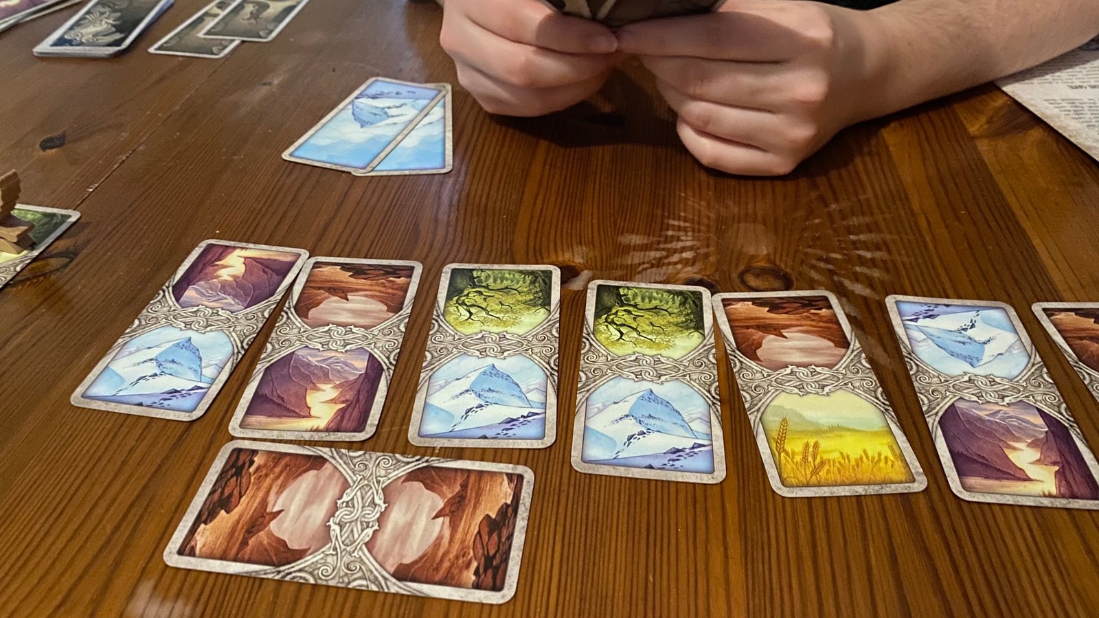 Hands grip cards from Odin's Ravens, with others laid out on a wooden surface