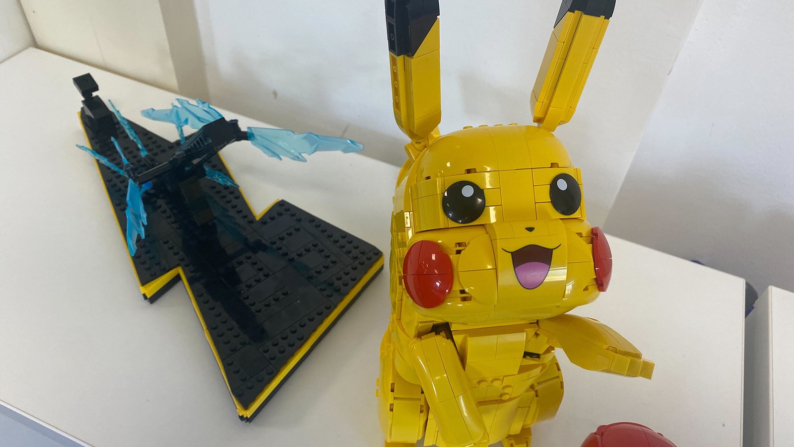 Lego Pikachu and Poke Ball set against a white background, with Pikachu looking up with the black stand behind it