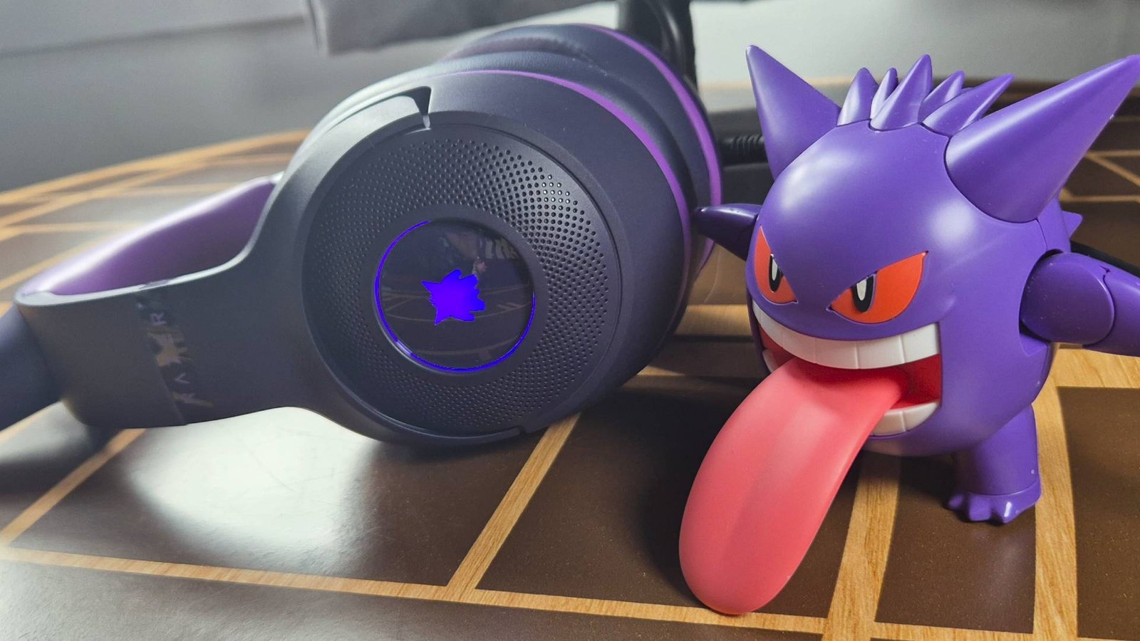 Photo of a purple headset laying on its side, with a purple toy of the Pokemon Gengar sitting to its right side.