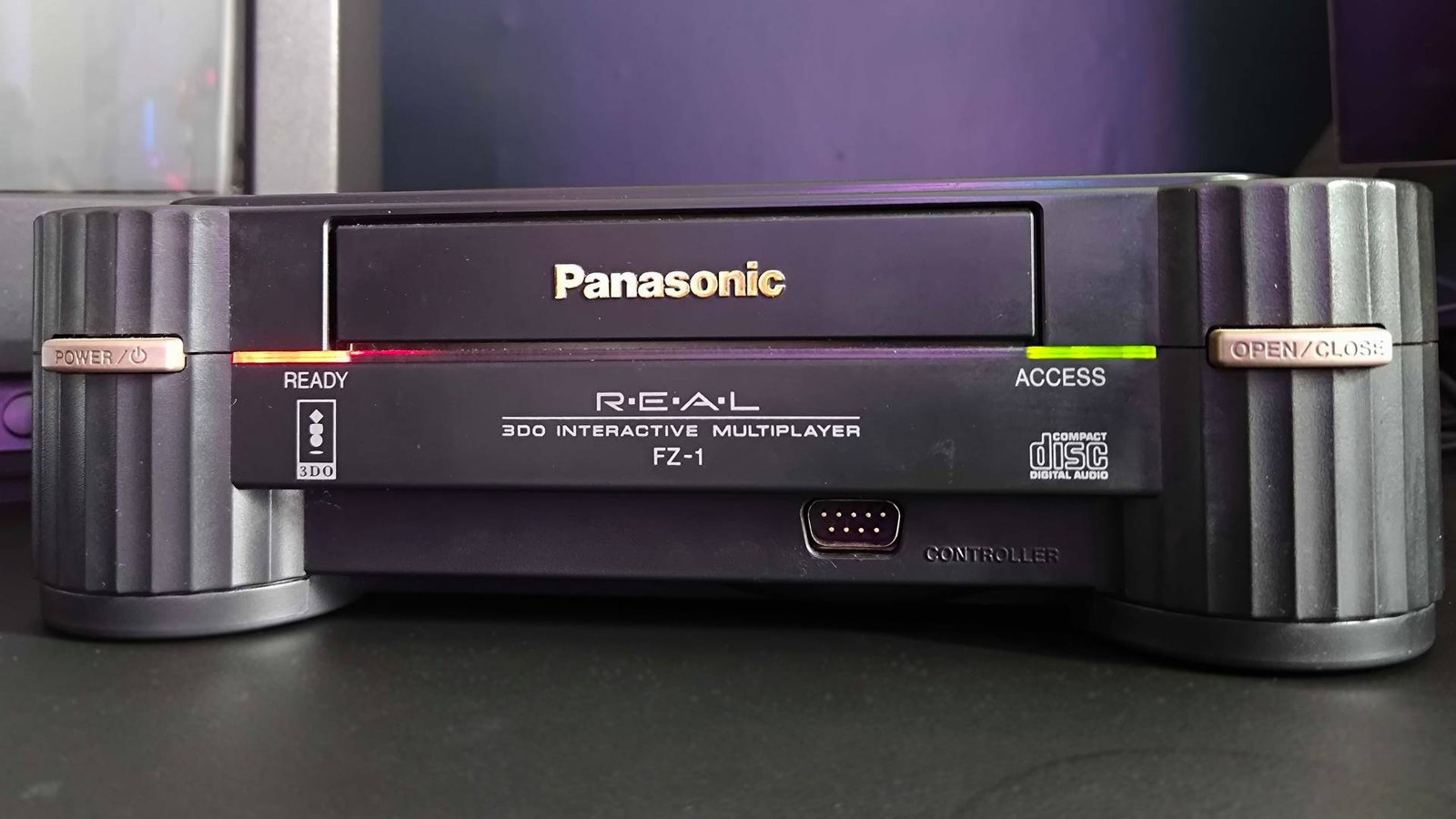 Close up of Panasonic 3DO console on black desk with red ready and green access lights illuminated.